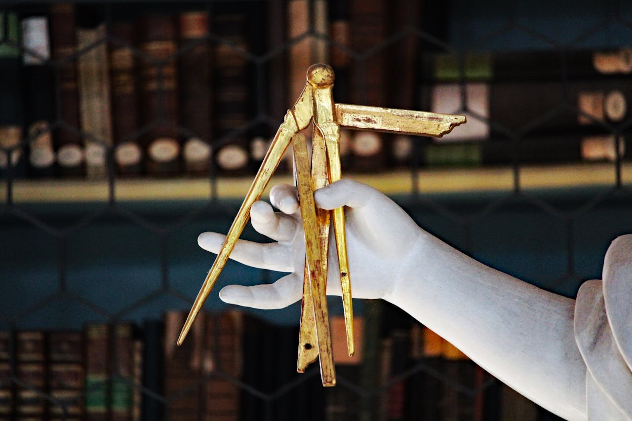 A detailed sculpture hand holding golden calipers in a classic library setting.